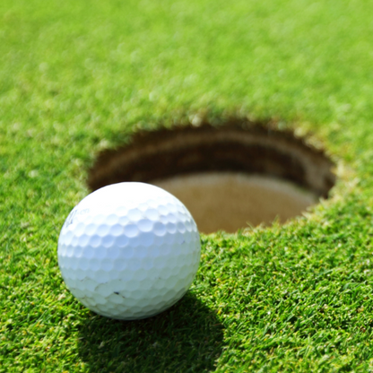 Golf ball on the green beside the hole representing a custom first tee golfer introduction voiceover announcement.